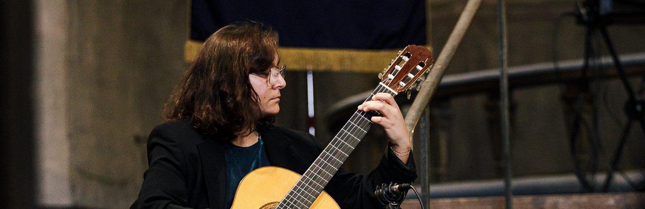 Gitarrist spelar klassisk gitarr på en konsert I Borgarhemmets kyrka med Stockholms Borgerskaps sigill i bakgrunden.